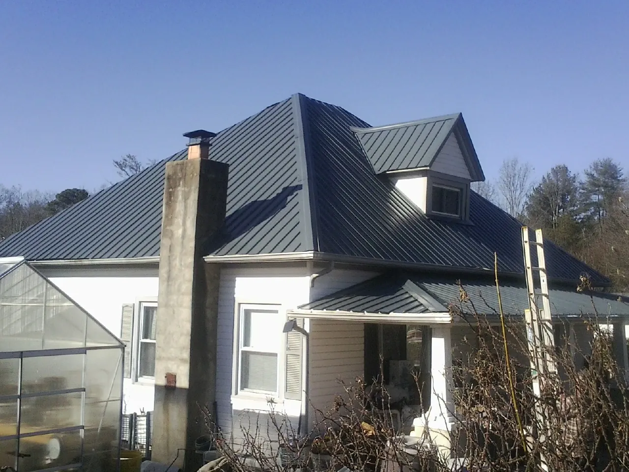 Dark blue standing seam metal roof on a white farmhouse with dormer — Slate & Tile Roof Repair by Roofing Brothers in Schwertner