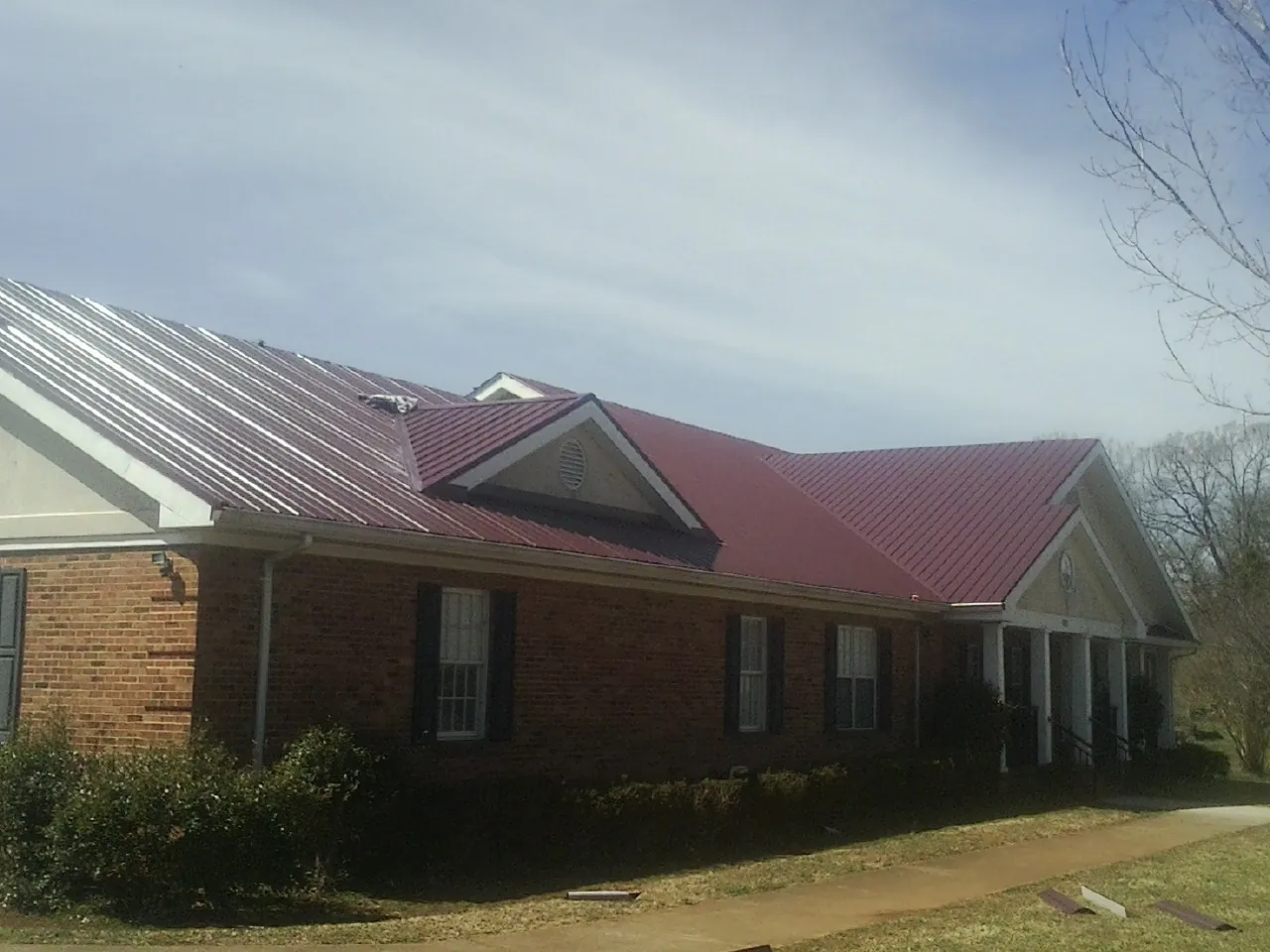 Red metal roof with gabled entries on a long brick building, from a Hail Damage Roof Repair job in Schwertner