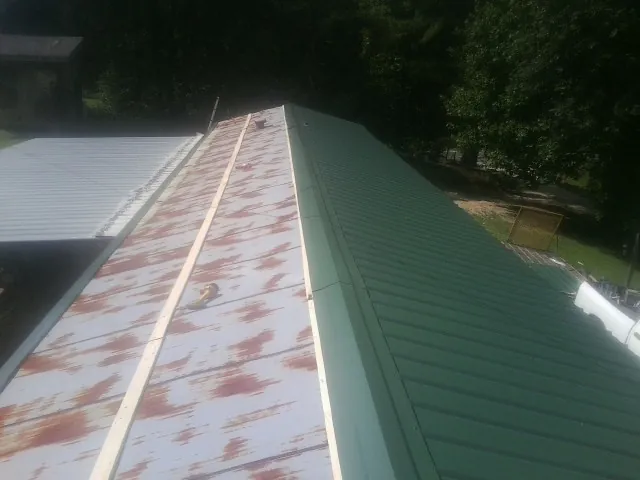 Old rusted panels beside newly installed green metal roofing — Wind Damage Roof Repair by Roofing Brothers in Schwertner