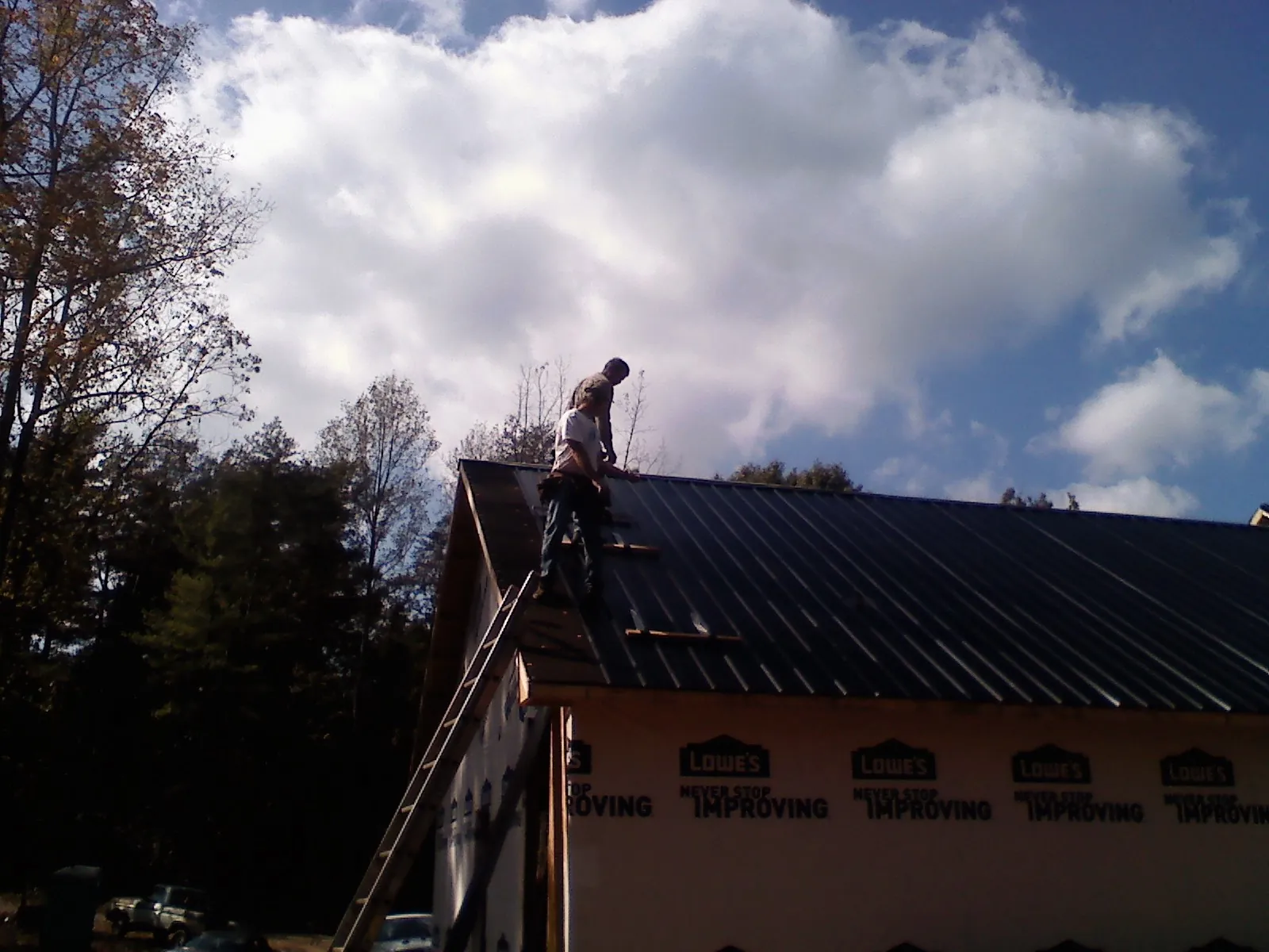 Roofer fastening dark metal panels high against a cloudy sky, from a Roof Inspection job in Schwertner