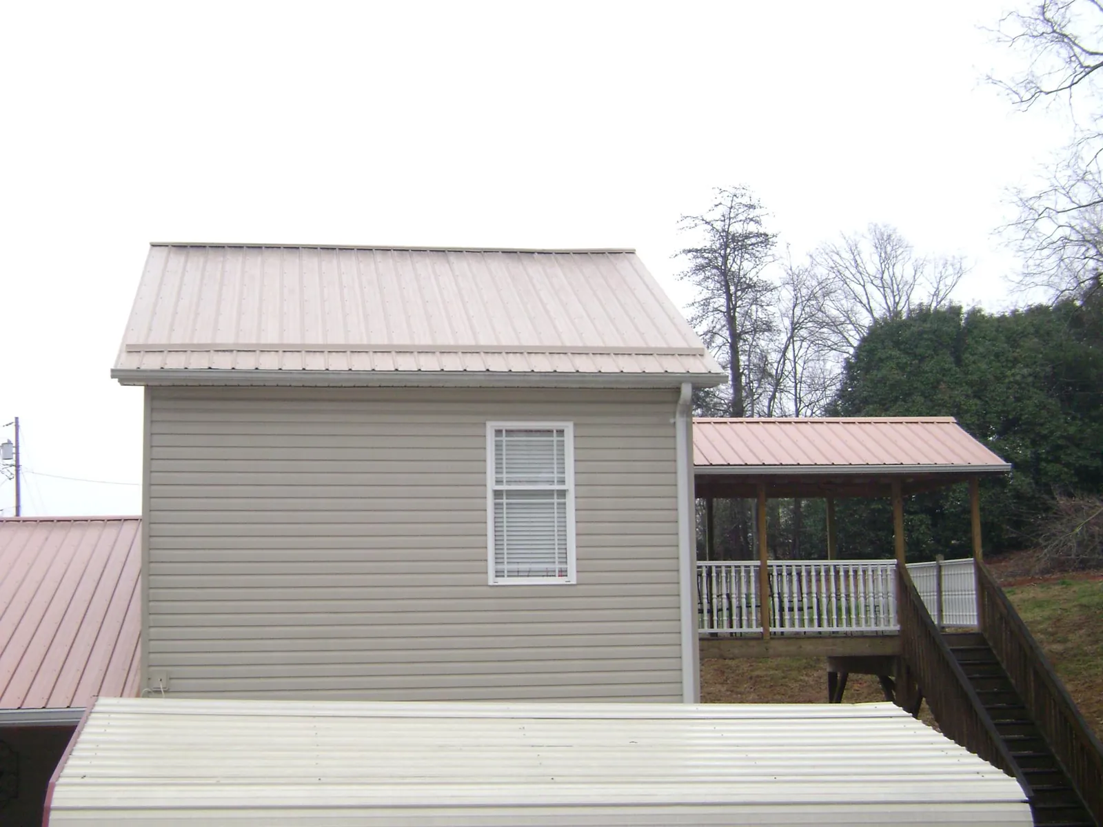 Tan metal roofs on a two story addition and attached porch, from a Roof Replacement job in Schwertner